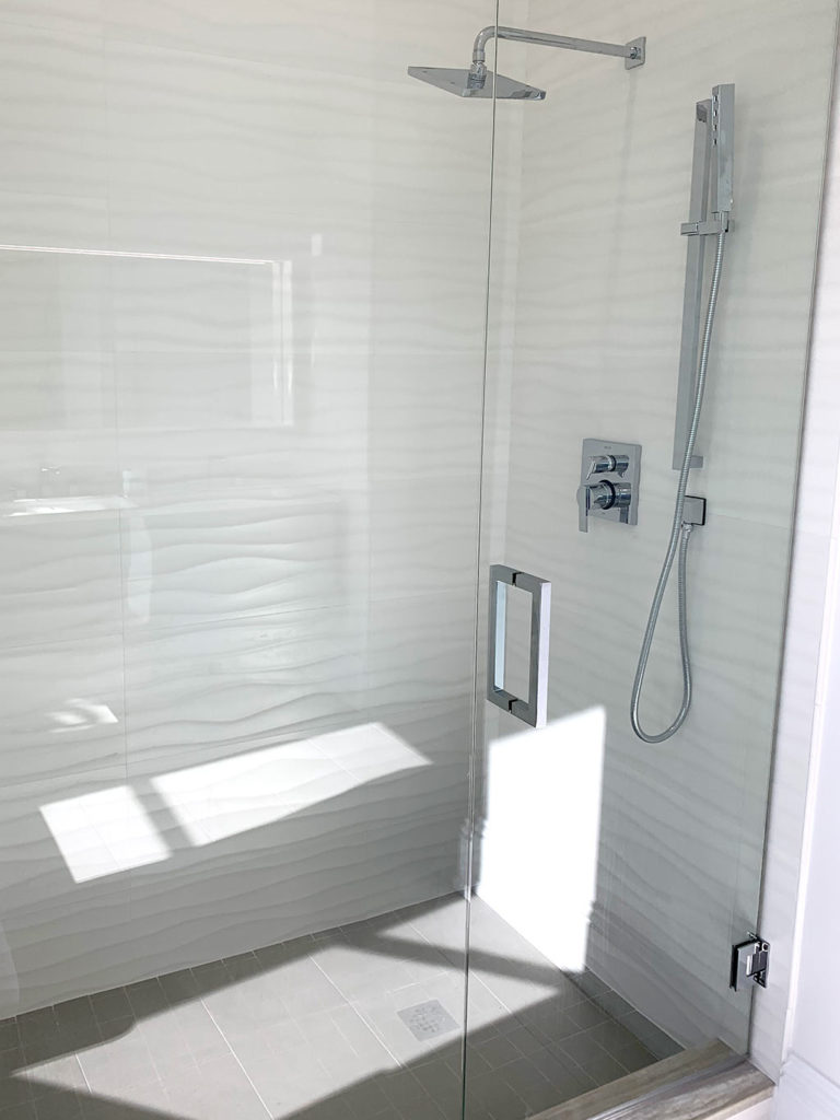 New glass shower enclosure with white wavy tile on shower walls