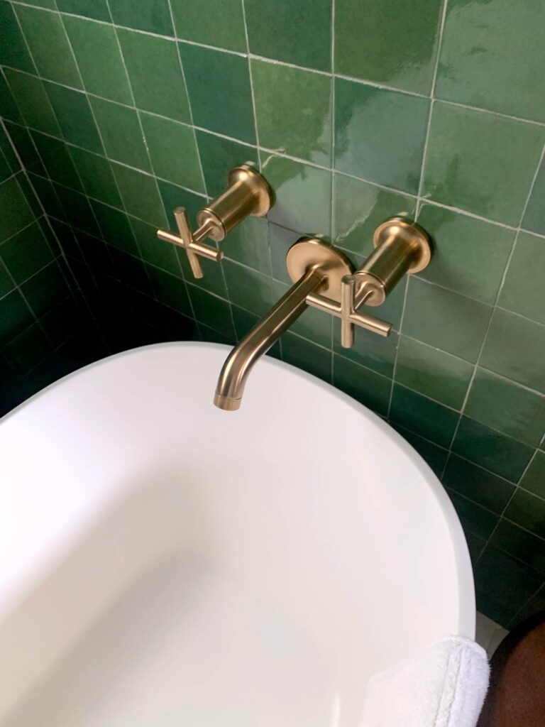 Closeup of brass wall-mounted bath taps over freestanding tub