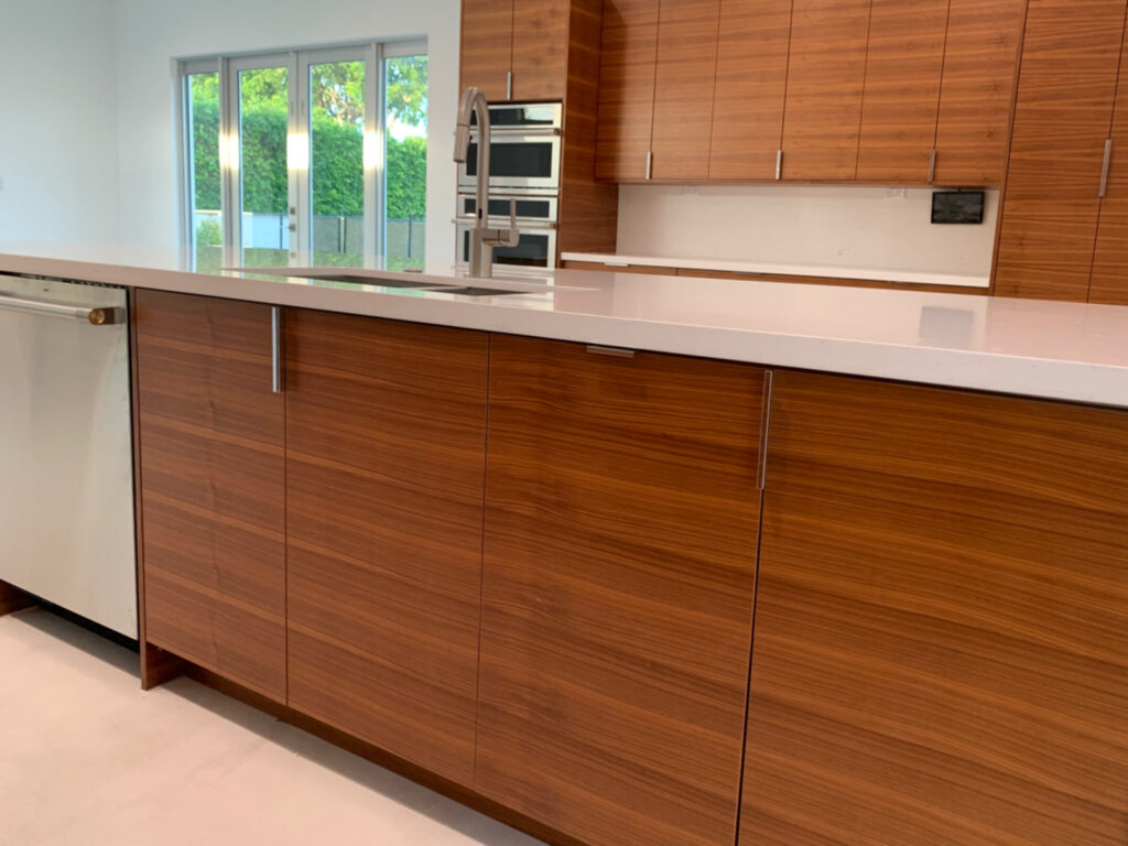 Closeup of island base cabinets with perimeter cabinets and double oven in the background